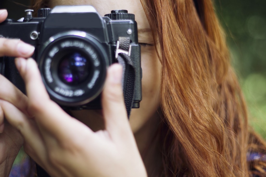 A woman with red hair using a camera, taking a photograph, adjusting the lens.